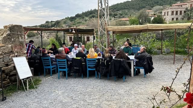Büyük grup Doğanbey köyü taş evler önünde açık hava sofrası