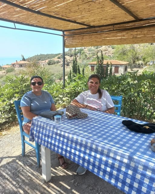 İki kadın hasır çatı altında mavi masa örtüsü deniz manzarası